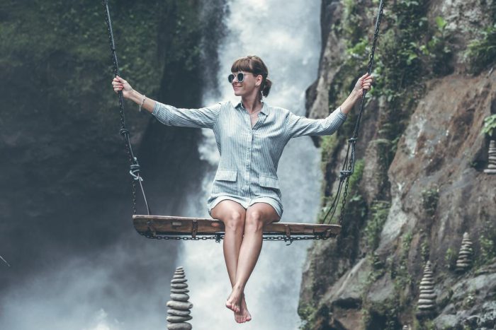 Femme sur une balançoire, avec derrière elle une cascade 