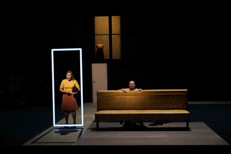 Décor d'un intérieur avec une femme debout et un homme accroupi derrière un canapé.