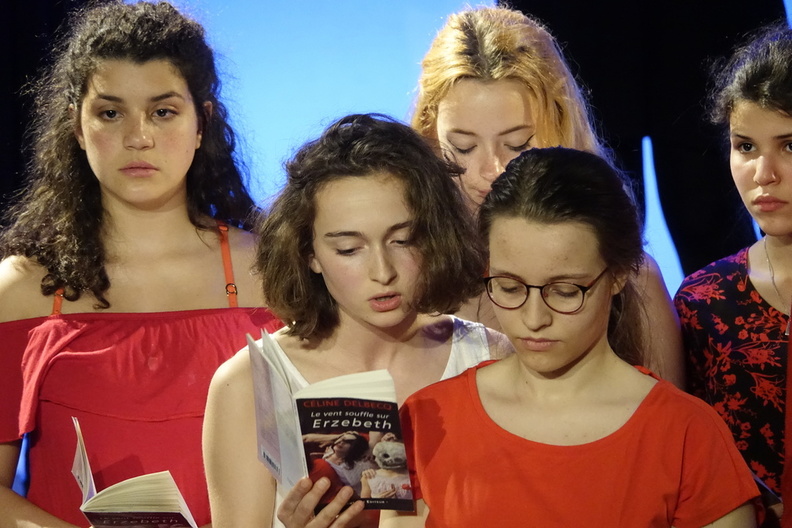 Une jeune comédienne lit une pièce de théâtre à l'oreille d'une autre jeune comédienne sur scène